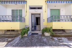 Un edificio amarillo con una entrada central, dos balcones con barandillas y plantas en macetas a cada lado.