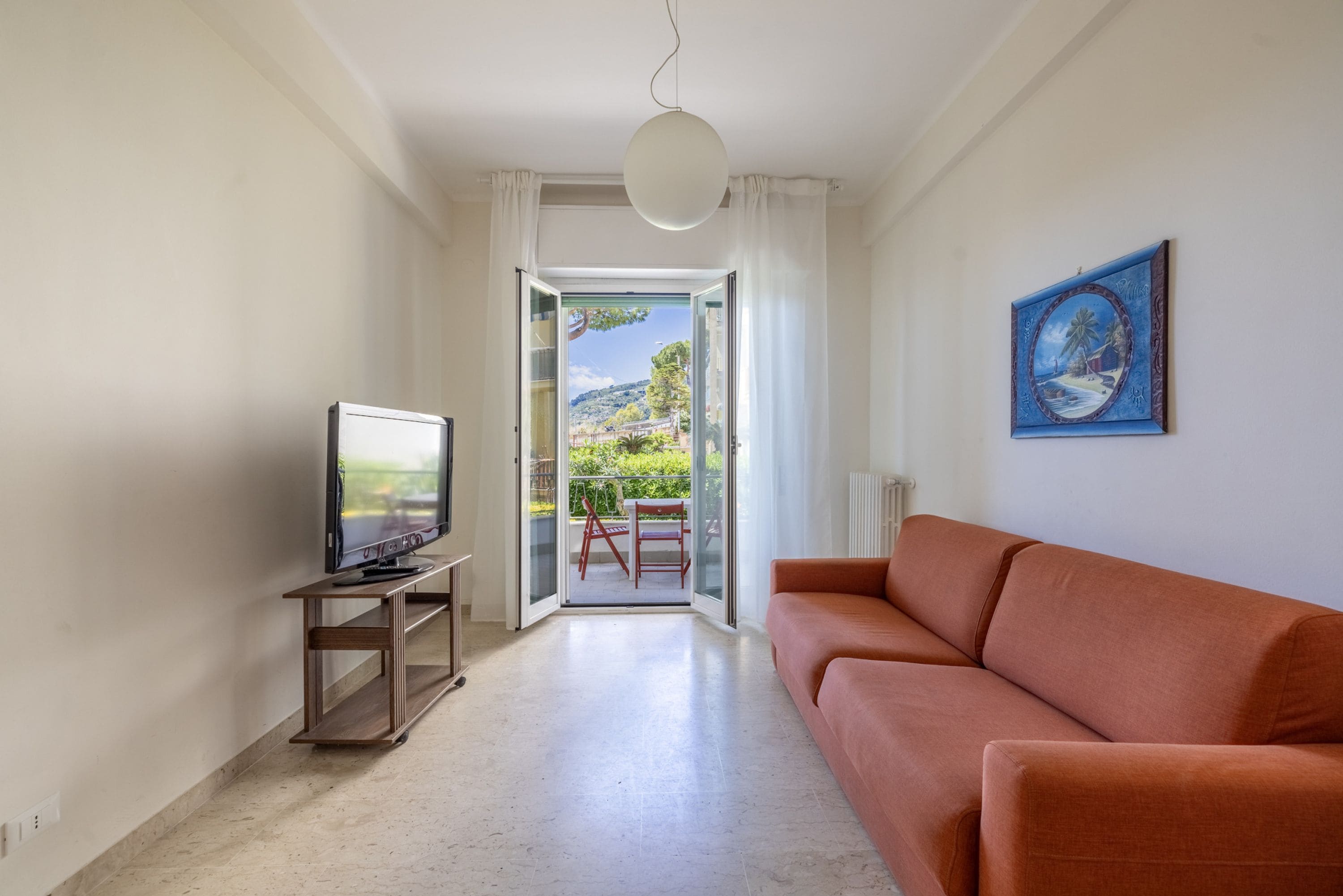 A living room with a television on a stand, a sofa, and a painting on the wall.