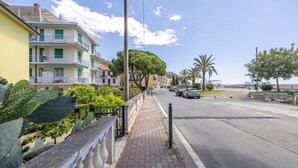 Una calle costera con edificios de varios pisos, aceras y coches aparcados.