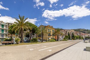 Ampia strada deserta fiancheggiata da edifici a più piani, palme e un cielo azzurro limpido.