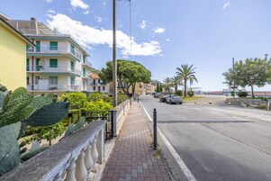 Una calle costera con edificios de varios pisos, aceras y coches aparcados.
