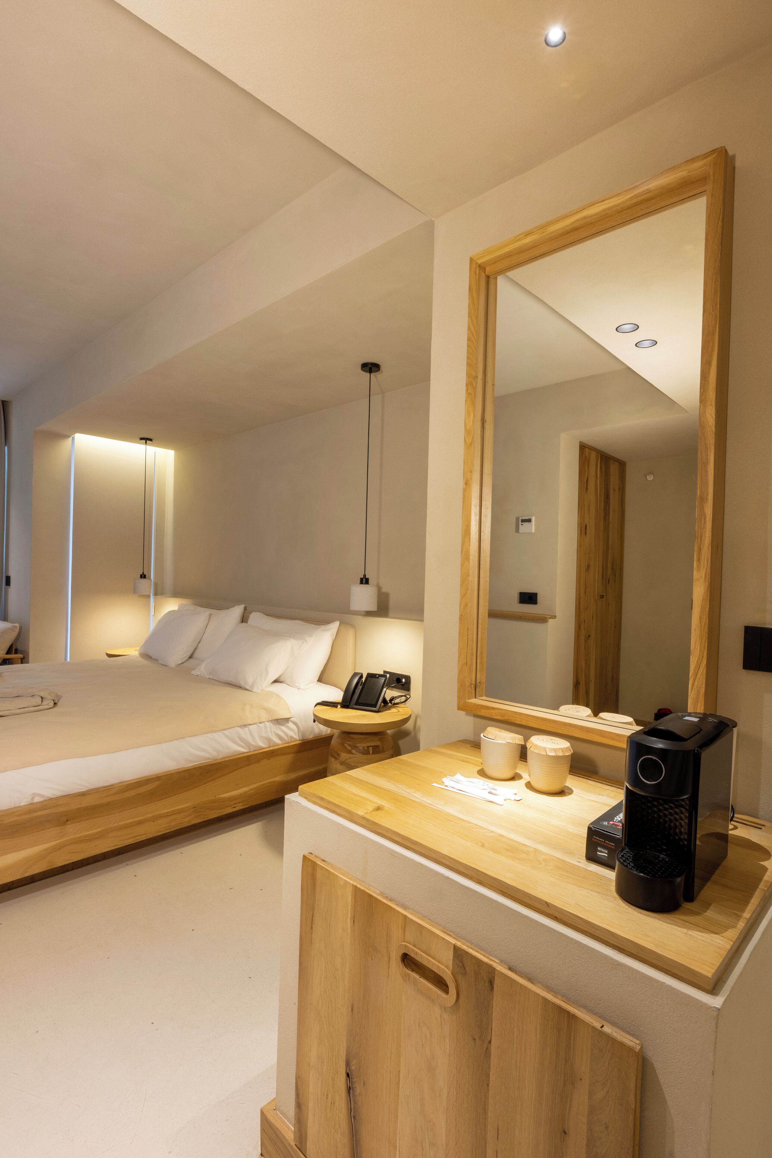 Una habitación de hotel moderna con una cama grande, una mesita de noche, cafetera y un espejo.