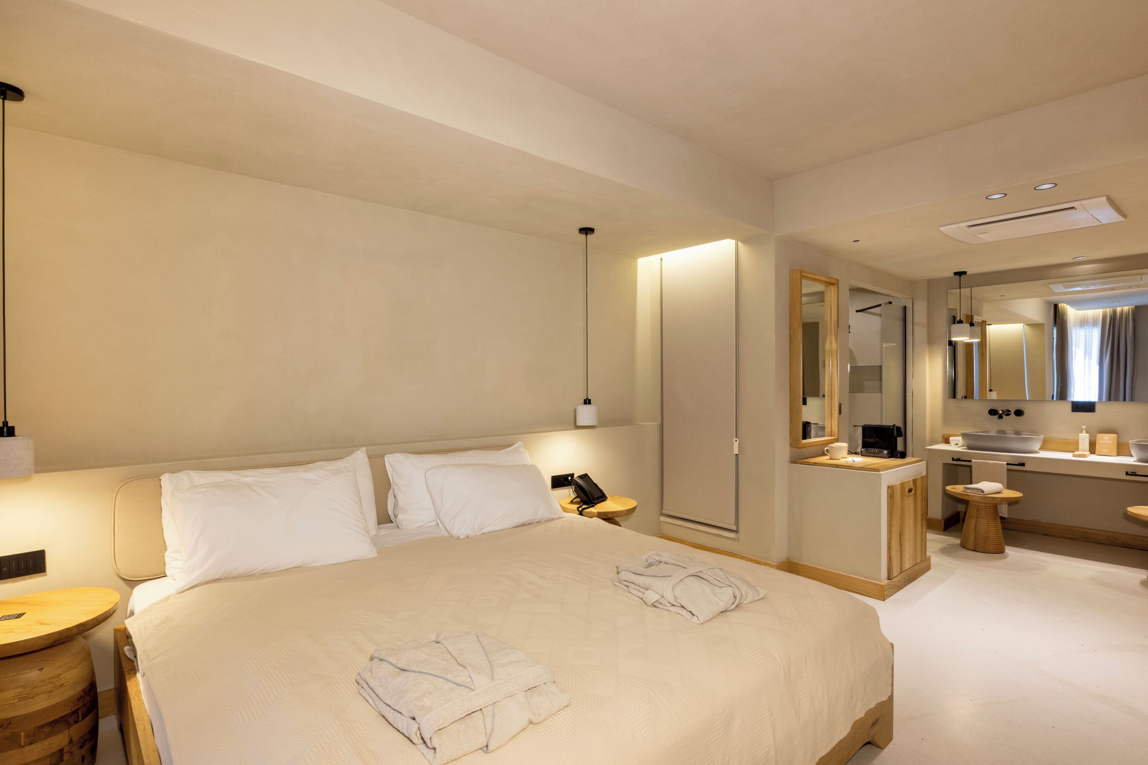 A hotel room with a large bed, bedside table, lamp, and a bathroom with a sink, mirror, and towel rack.