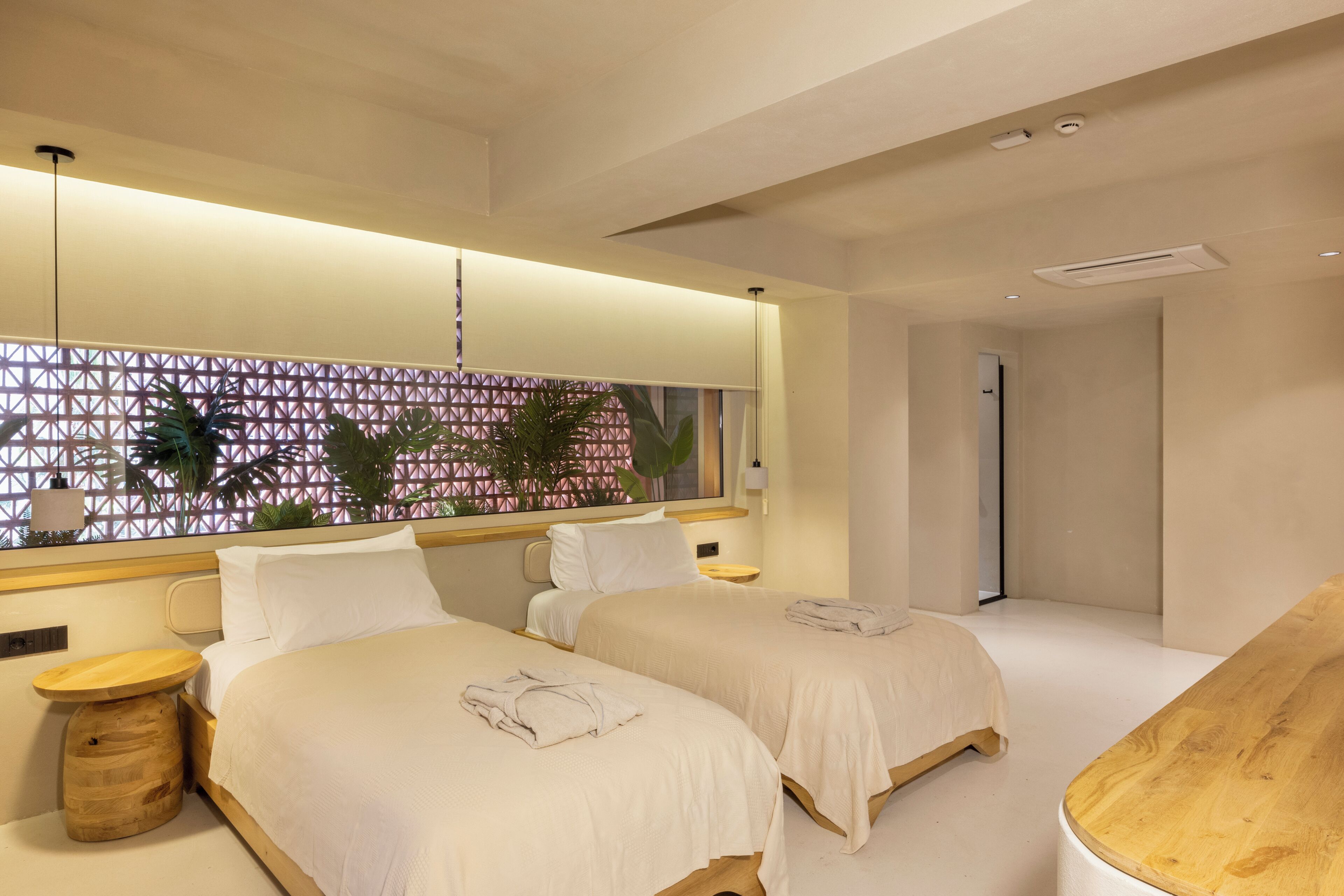 Una habitación de hotel moderna con dos camas, un ventanal con diseño geométrico y una mesita de noche de madera.