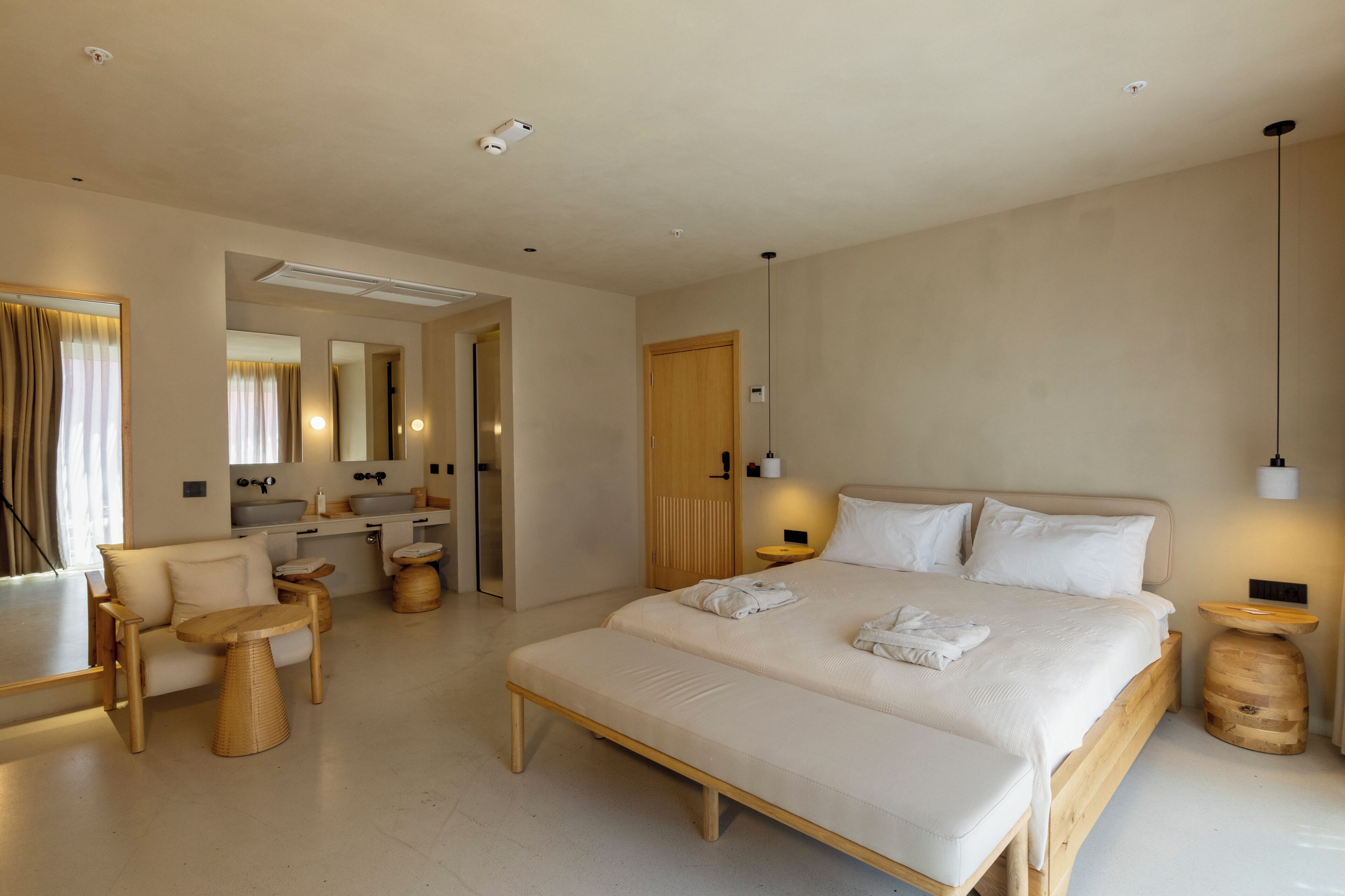 Une chambre d’hôtel moderne avec un grand lit, un canapé, une petite table ronde, une coiffeuse avec un miroir et une porte en bois.