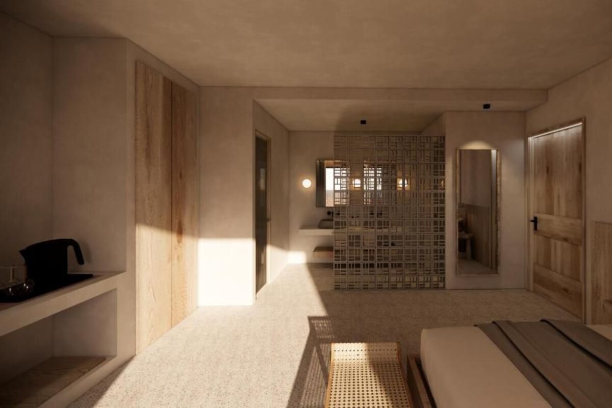 Habitación de hotel con cama, mesita de noche, lámpara y vista a un pasillo con separador de madera.