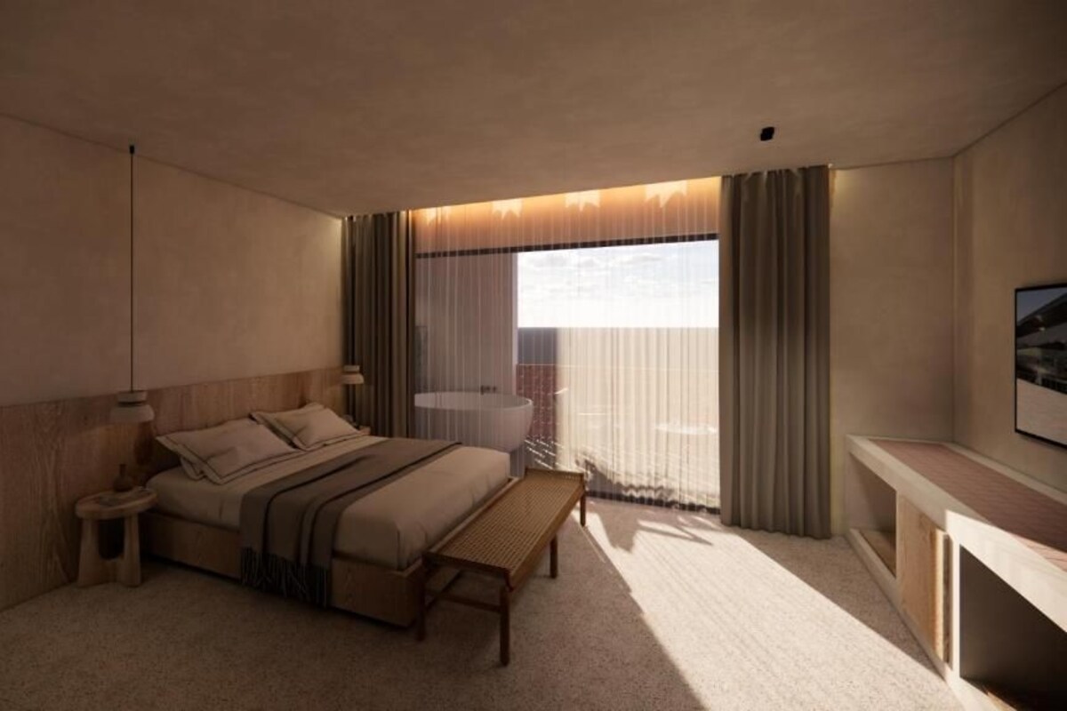Habitación de hotel moderna con una cama grande, mesita de noche y vista a la ciudad a través de cortinas translúcidas.