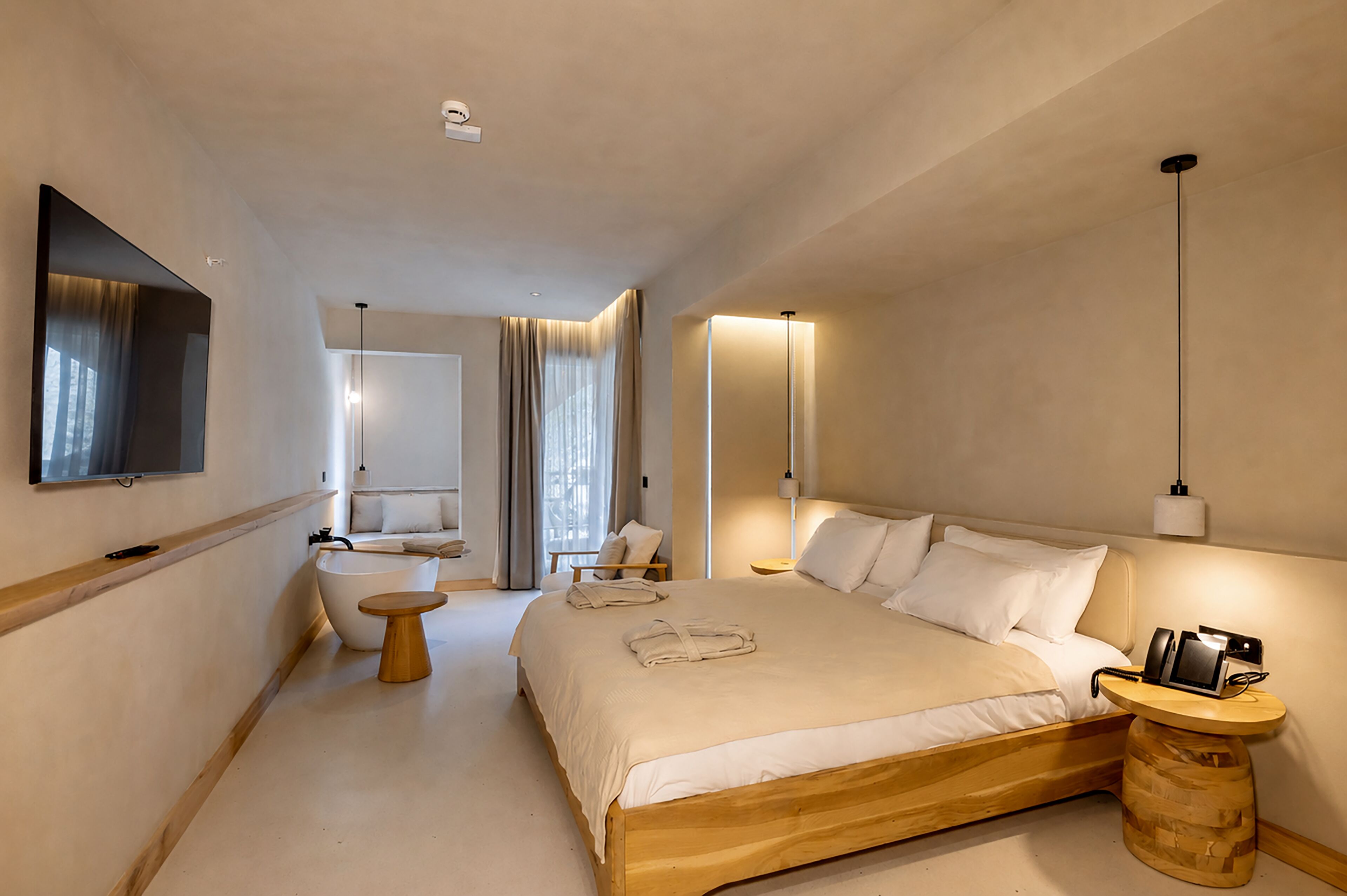 Habitación de hotel con una cama grande, mesita de noche, televisor de pantalla plana y baño con bañera e inodoro.