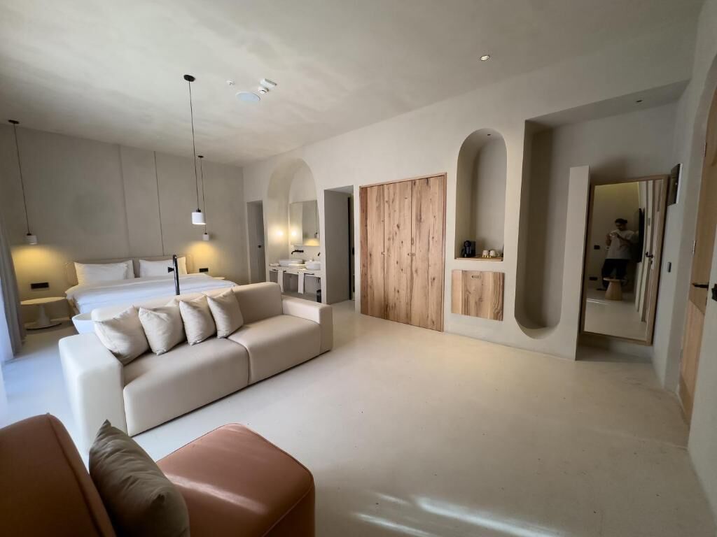 Un dormitorio moderno con una cama grande, un sofá, un armario de madera y un espejo.