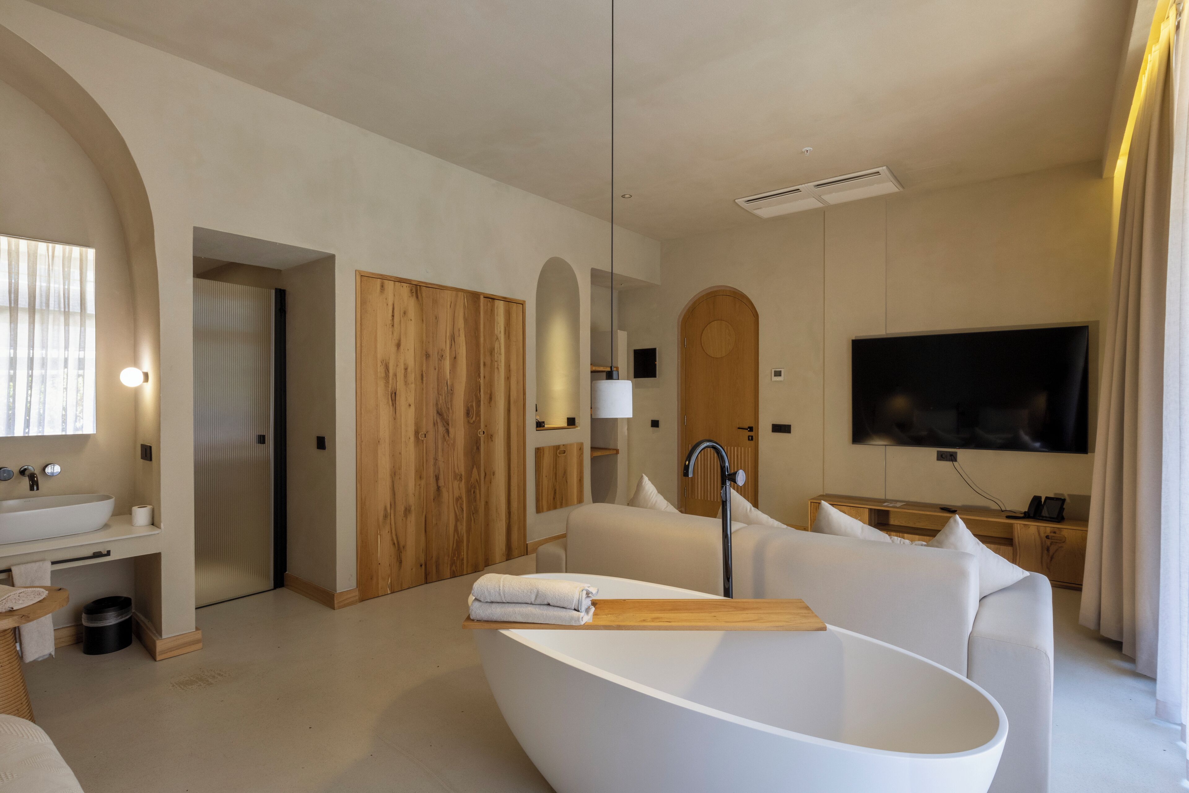 A modern bathroom with a freestanding bathtub, a large mirror, and a television mounted on the wall.