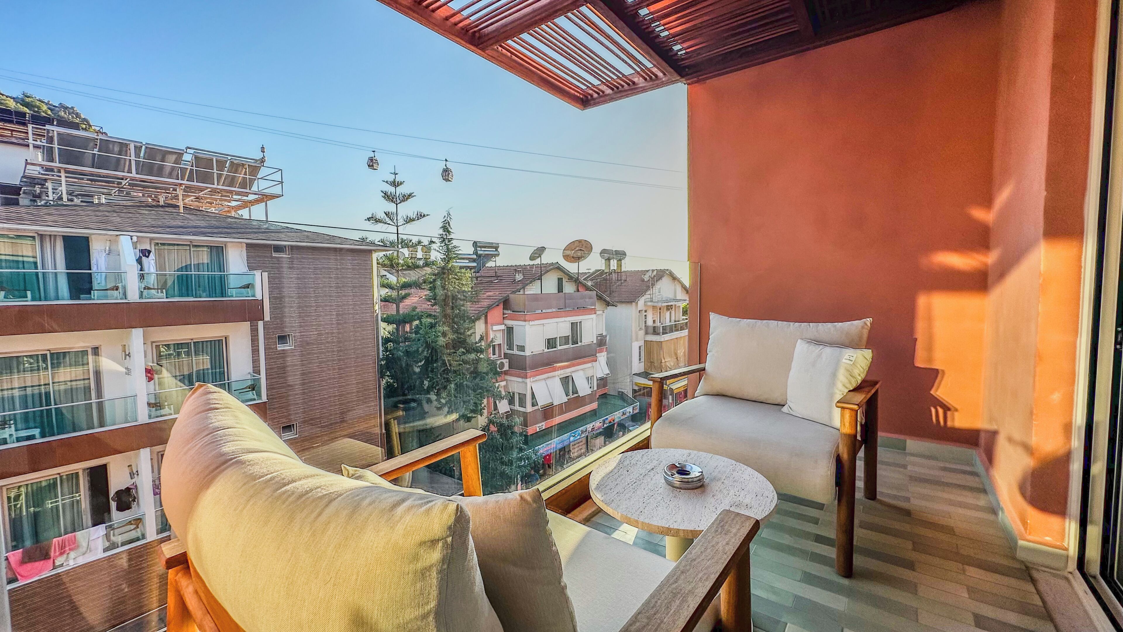 A balcony with a sofa, a small table, and a chair, overlooking a residential area with houses and trees.