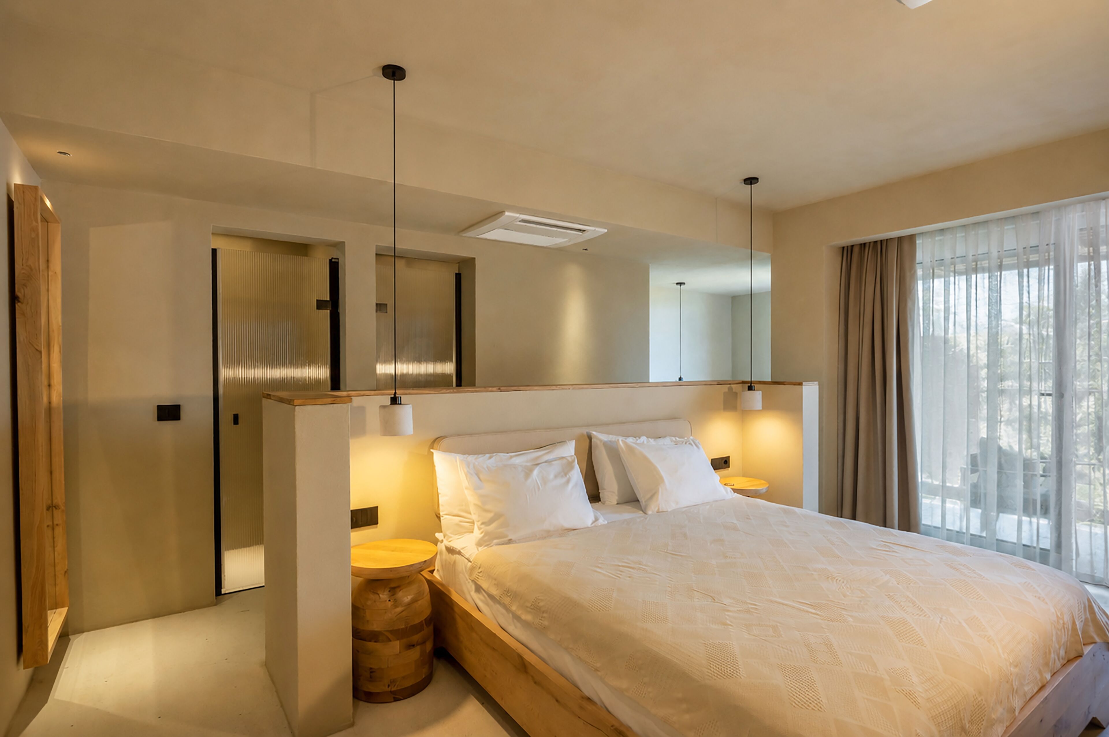 A modern hotel room with a large bed, a wooden headboard, a ceiling light, a bedside table, and a window with curtains.
