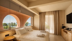 Una habitación de hotel moderna con una cama grande, un escritorio, un televisor y vista al mar.