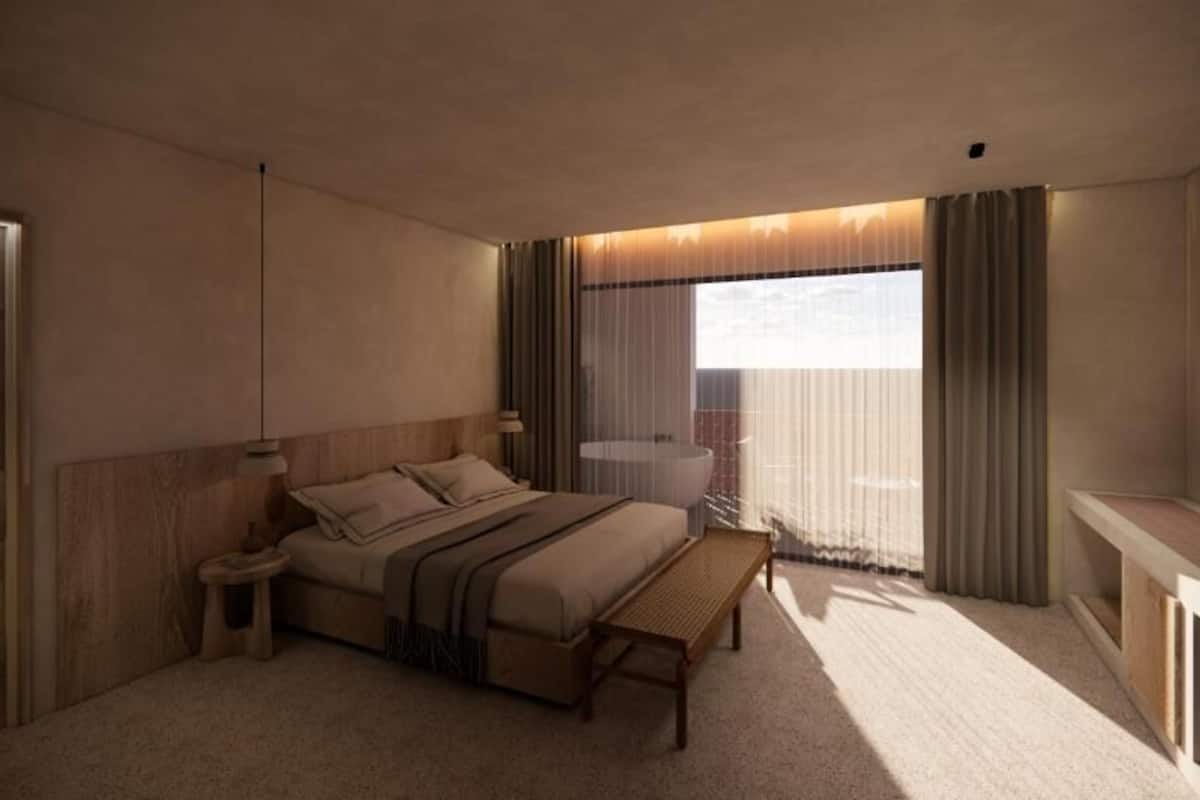Een moderne hotelkamer met een groot bed, nachtkastje en uitzicht op de stad door dunne gordijnen.