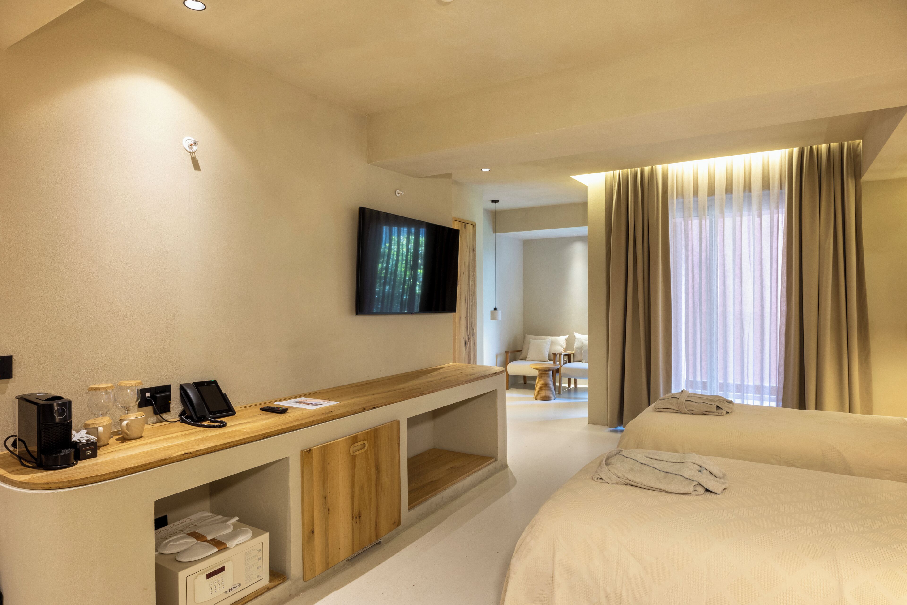 A hotel room with a wooden desk, a bed, a TV mounted on the wall, and a window with curtains.