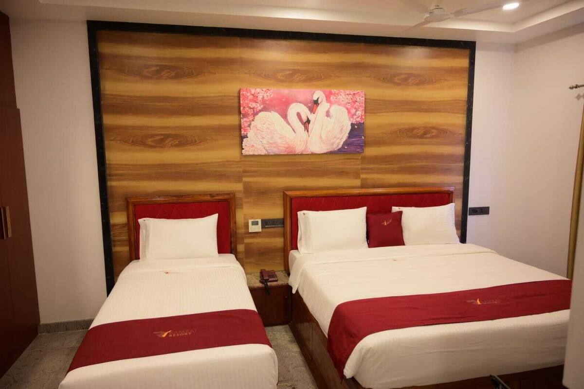 Een hotelkamer met twee bedden, elk met rode hoofdeinden en witte beddengoed. Boven de bedden hangt een schilderij van zwanen.