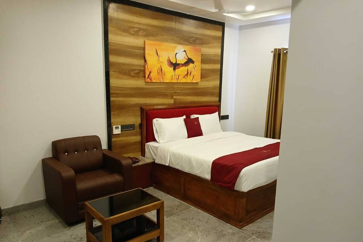 Hotelkamer met een bed, een bruine leren fauteuil, een klein houten tafeltje en een wand met een houten paneel en een schilderij van vogels.