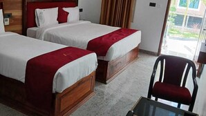 Habitación de hotel con dos camas, un cabecero de madera, una silla roja, una mesita pequeña y un cuadro de caballos en la pared.