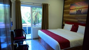 Habitación de hotel con cama, una silla, ventana con cortinas y un cuadro en la pared.