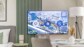 A modern hotel room with a large TV displaying a cityscape, a small round table with a lamp, a green-striped wall, and a framed artwork. - CoView Pirna - Altstadt - Parkplatz (Pirna)