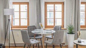 A dining area with a round table, four grey upholstered chairs, a white vase with flowers, and a potted plant. - CoView Pirna - Altstadt - Parkplatz (Pirna)