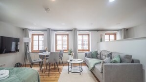 A modern, well-lit room with a bed, a sofa, a dining table with chairs, and a TV mounted on the wall. - CoView Pirna - Altstadt - Parkplatz (Pirna)