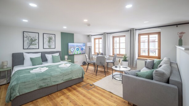 A modern hotel room with a large bed, a grey sofa, a dining table with chairs, and a TV mounted on the wall. - CoView Pirna - Altstadt - Parkplatz (Pirna)