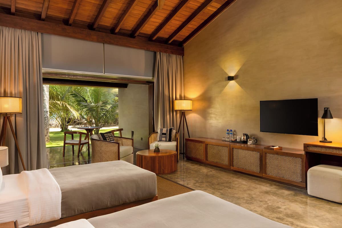 A hotel room with two beds, a TV, a sofa, a round coffee table, and a view of the outdoors.