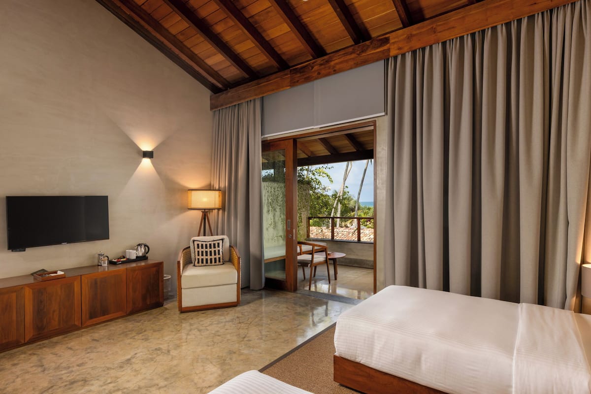 A hotel room with a wooden ceiling, a flat-screen TV, a sofa, a bed, a dining table, and a view of the outdoors.
