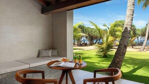 A patio with a round table, two wooden chairs, a sofa, and a view of a tropical garden with palm trees. - Villa Thamburu (Bentota)