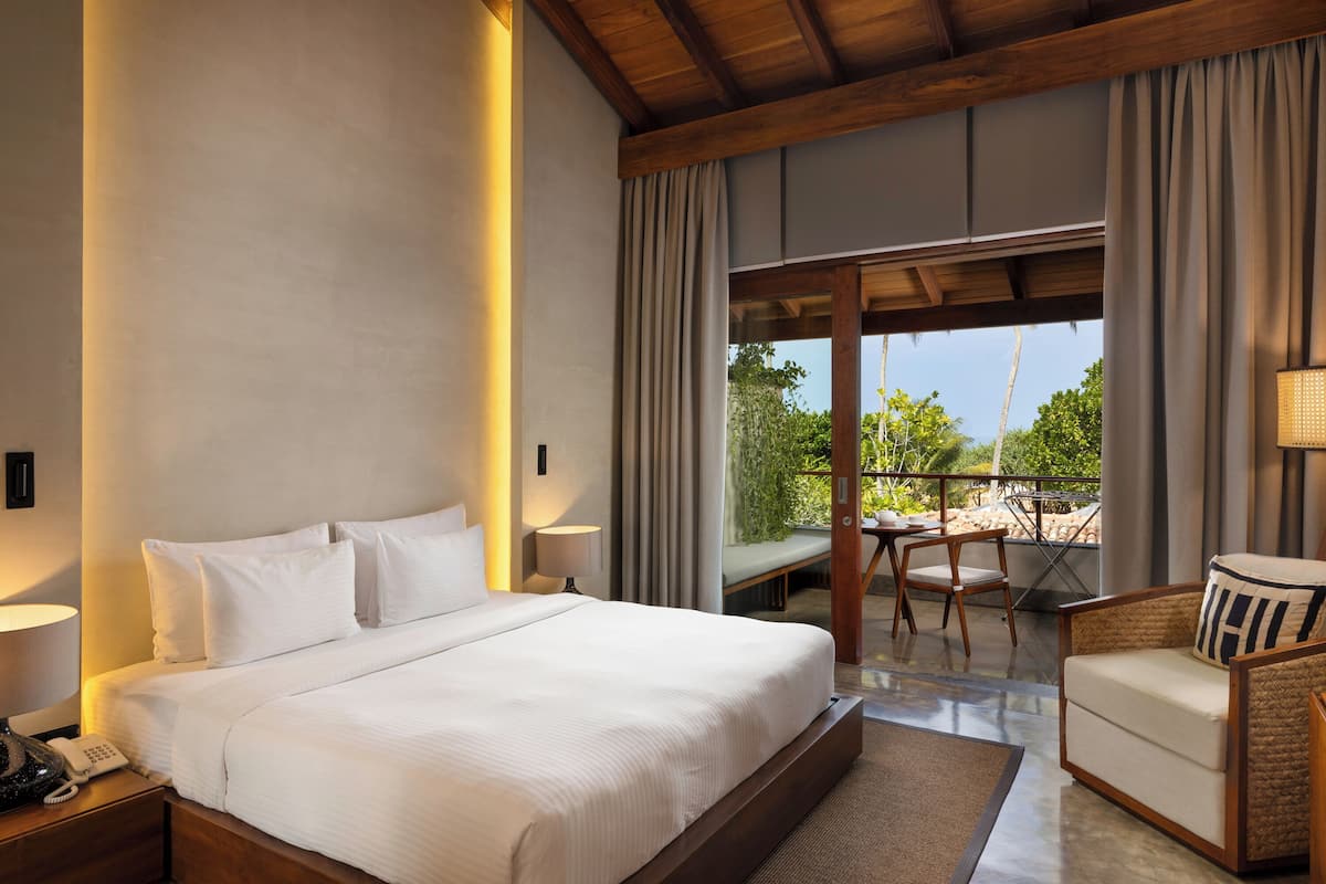 A hotel room with a large bed, a desk with a phone, a chair, and a view of the outdoors.