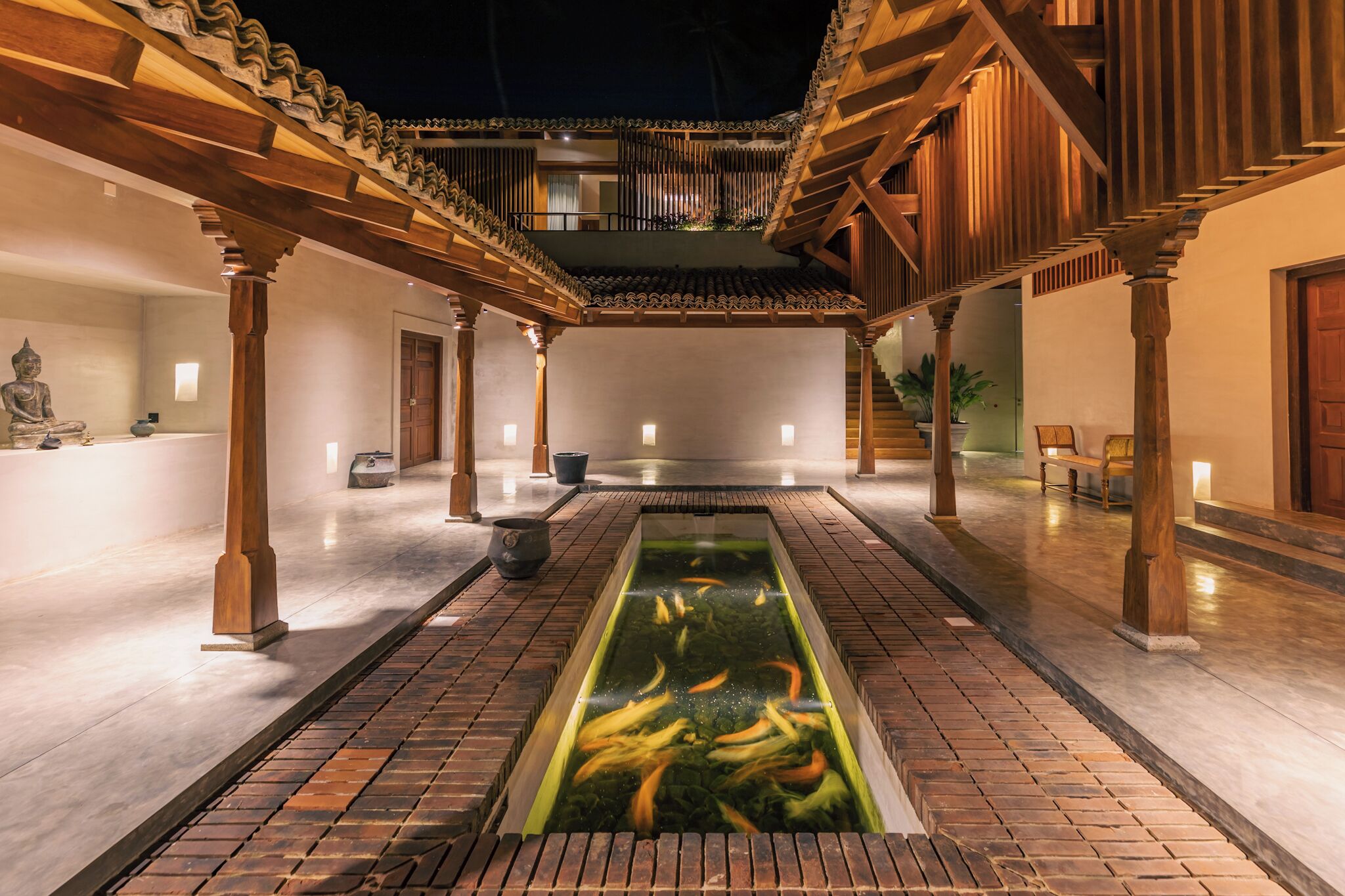 A courtyard with a koi pond, wooden pillars, and a statue.
