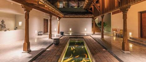 A courtyard with a koi pond, wooden pillars, and a statue.