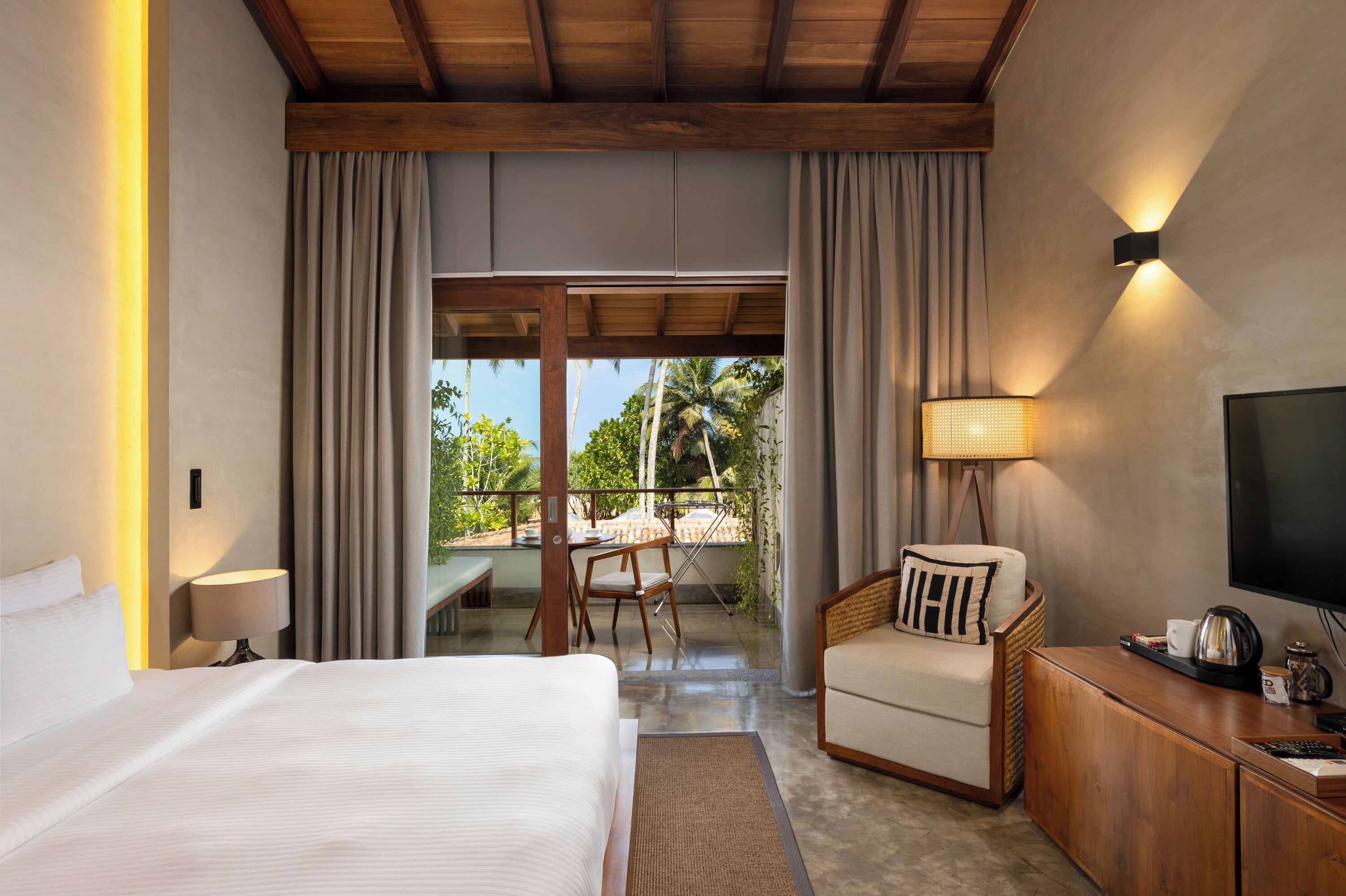 A hotel room with a bed, a chair, a TV, a lamp, and a view of the outdoors.