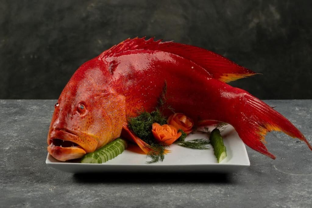 A fish carved into a decorative piece on a white plate with vegetables and herbs.