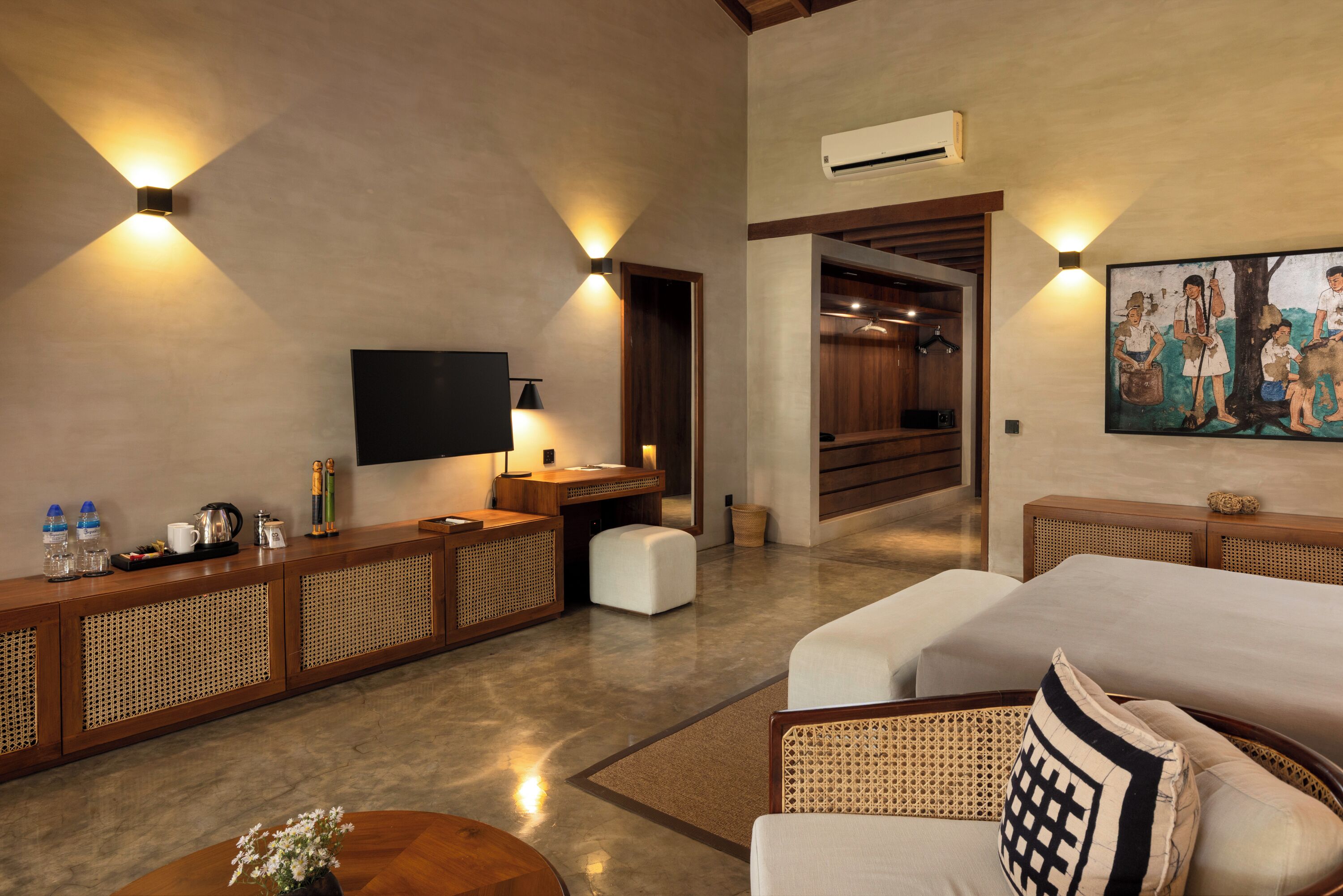 A modern hotel room with a flat-screen TV, a wooden console table with amenities, a large bed, and a painting on the wall.