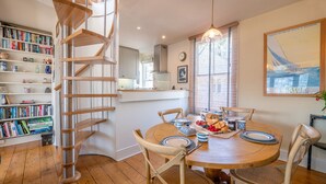 A dining area with a wooden table, chairs, and a spiral staircase. - Dartmouth Hideaway, Large Roof Terrace & Views (Dartmouth)