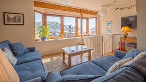 A cozy living room with a large window, a telescope, and a view of a hillside. - Dartmouth Hideaway, Large Roof Terrace & Views (Dartmouth)
