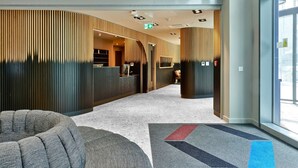 A modern hotel lobby with a reception desk, seating area, and a large window.