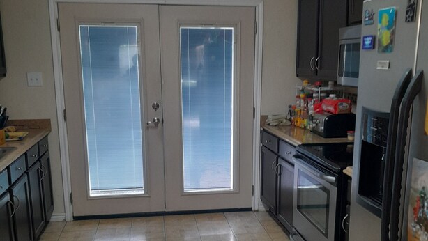 Una cocina equipada con refrigerador, horno, microondas y puertas dobles con ventanas.