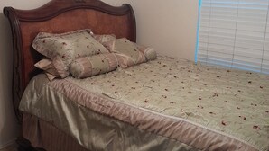 Un dormitorio con cabecera de madera, ropa de cama floral y una ventana con persianas.