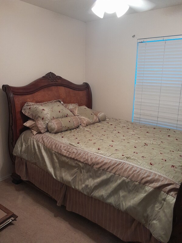Un dormitorio con cabecera de madera, ropa de cama floral y una ventana con persianas.