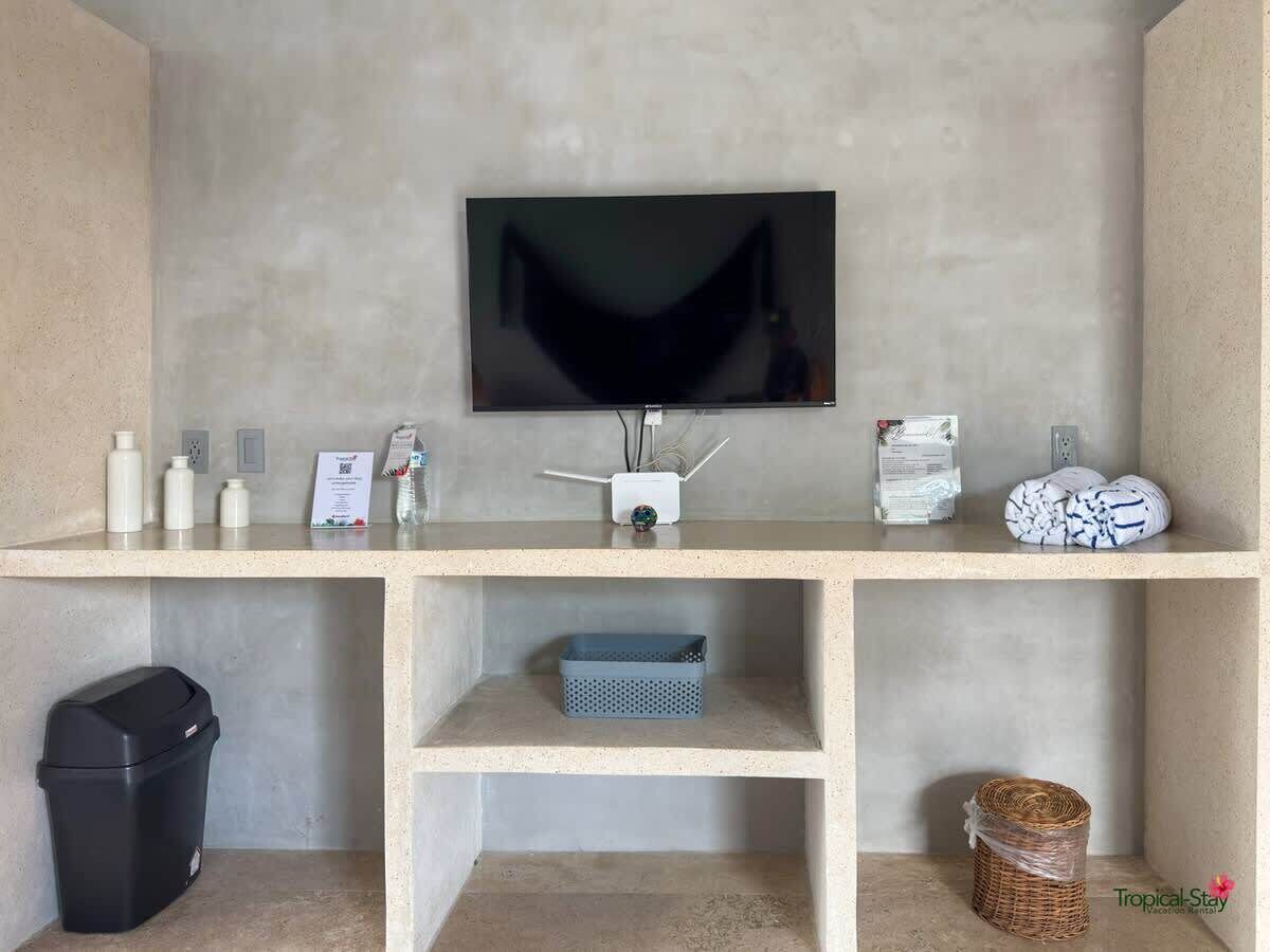 A modern room with a flat-screen TV mounted on a wall, a small desk with a white router, and a trash bin.