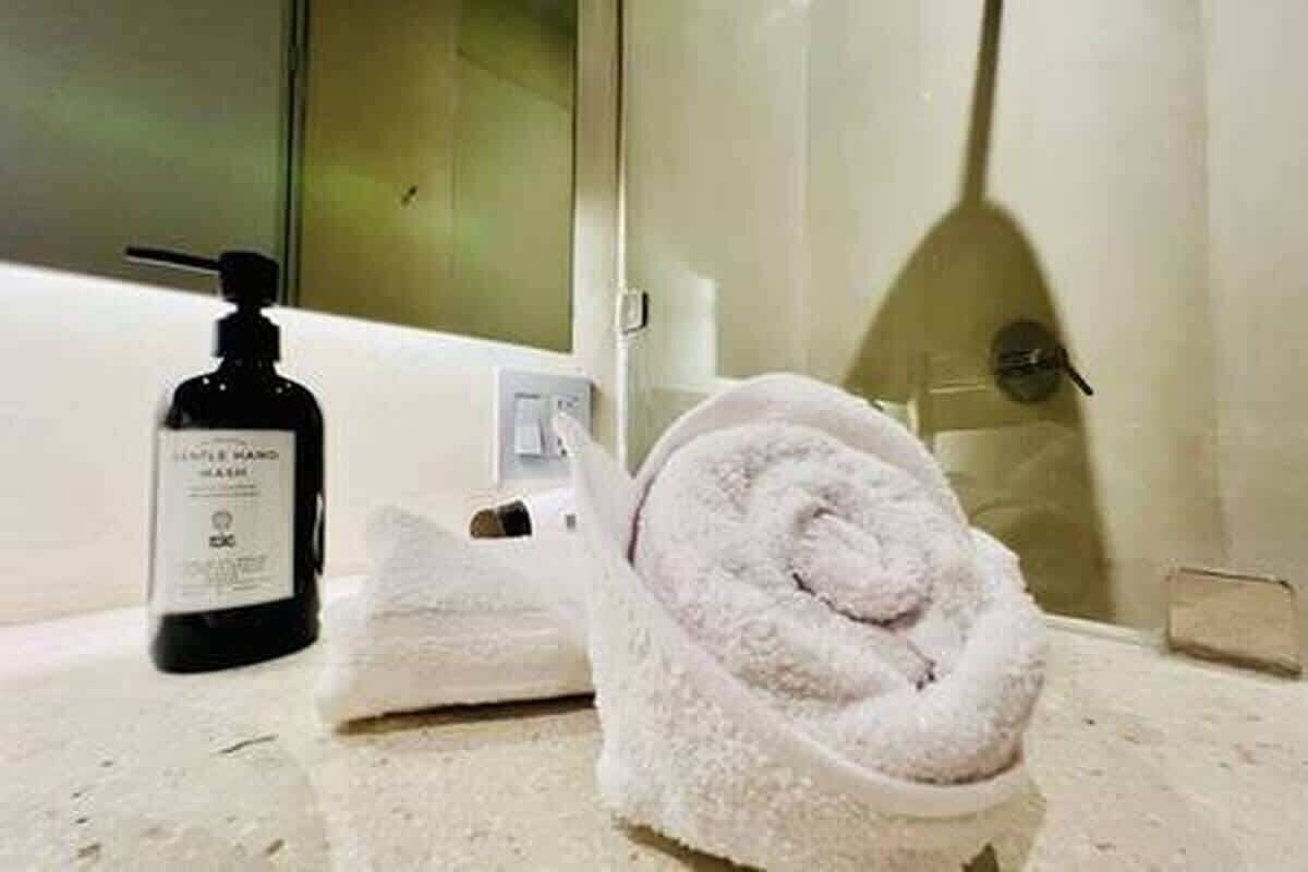 A bathroom with a white sink, a bottle of hand soap, and a rolled towel on the counter.