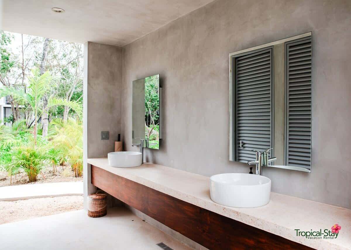 Une salle de bain moderne avec deux lavabos, un grand miroir et une fenêtre avec des volets.