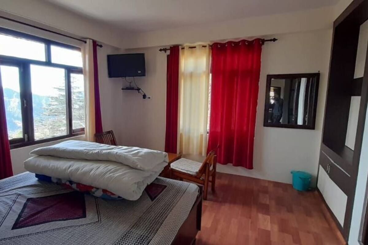 Quarto com cama, televisão, cadeira, janela com cortinas e porta.