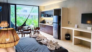 A modern hotel room with a large bed, a dining area with a hammock, a kitchenette, and a TV.