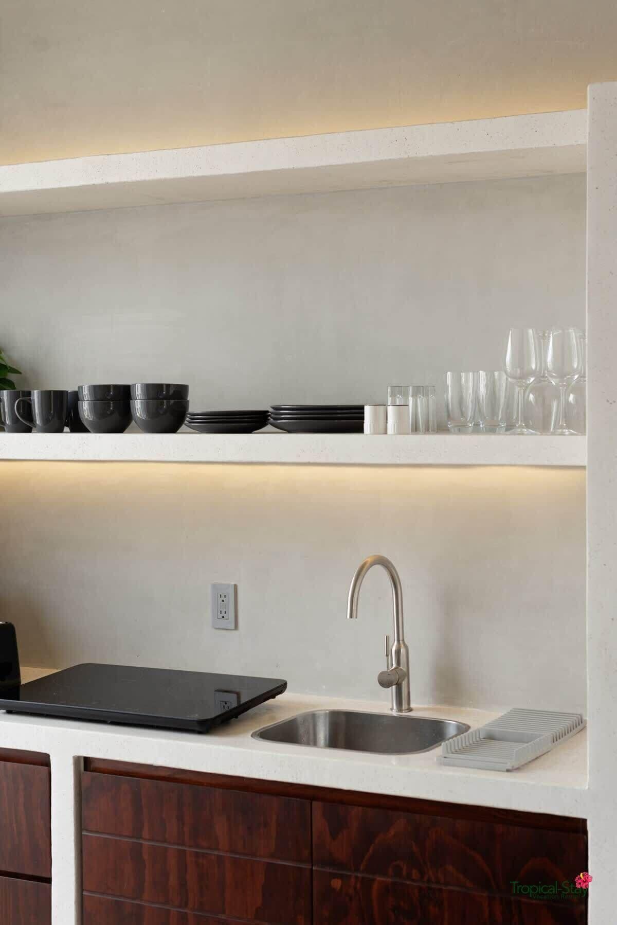 A modern kitchen with a stainless steel sink, a black cutting board, and various kitchenware on white shelves.