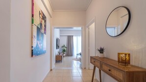 A hallway with a wooden console table, a round mirror, and a large painting on the wall. - Residence City Frida (Rodos)