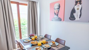 A dining table set with breakfast items, a window with curtains, and two wall art pieces. - Residence City Frida (Rodos)